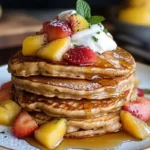A stack of vibrant purple taro pancakes topped with fresh fruit, a drizzle of honey, and whipped cream, served on a white plate.